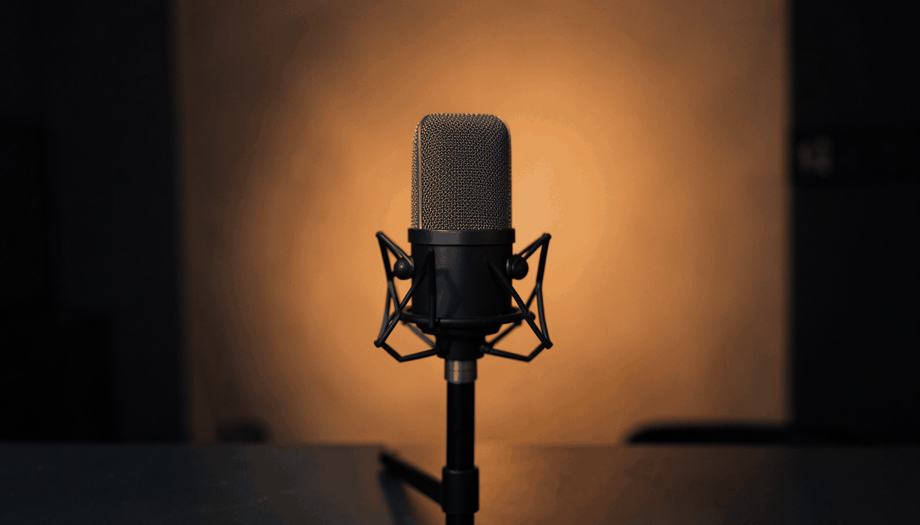 A minimalist podcasting setup in deep charcoal and warm orange tones, with a microphone centered against a softly lit backdrop